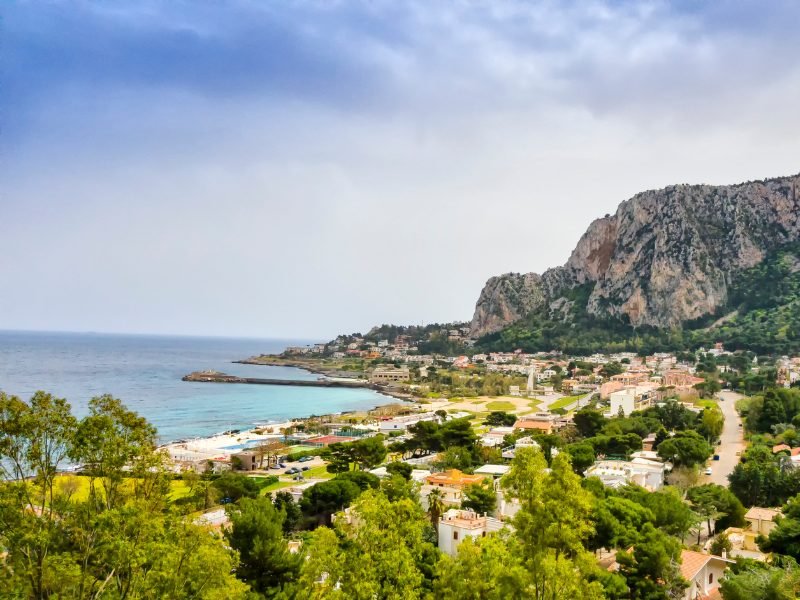 The town and rocky coastline near Spiaggia dell'Addaura, a popular beach near Palermo that is less busy than Mondello. Town, mountain, beach, and trees.
