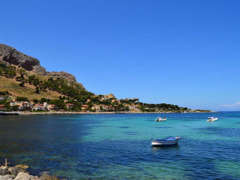 A beautiful coastline near Palermo, Italy best accessed if you are renting a car in Italy. Boat, mountain landscape, teal and dark blue sea.