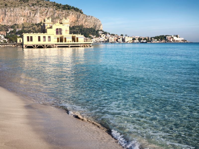 The beautiful clear blue waters of Mondello Beach near Palermo, Sicily, with a lido bathing establishment and town in the background