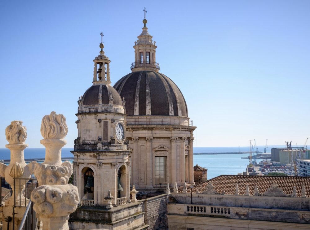 View of Catania's church with its clock and the marina in the background with cranes and parked cars