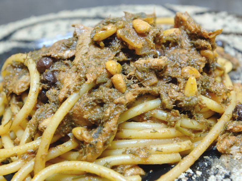 Bucatini noodles that look like spaghetti, with a paste-like tomato sauce where you can see pine nuts and raisins as part of the sauce.