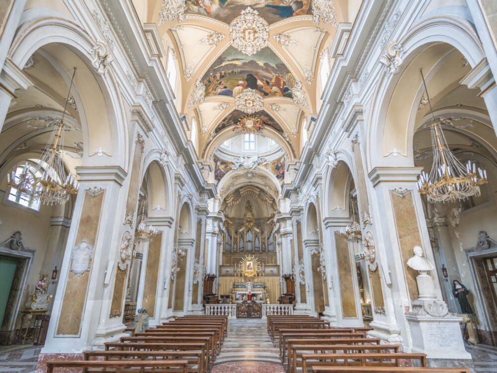 Interior of the stunning Basilica della Collegiata, which has a vaulted ceiling and frescoes that are very colorful, as well as an altarpiece and statues and busts