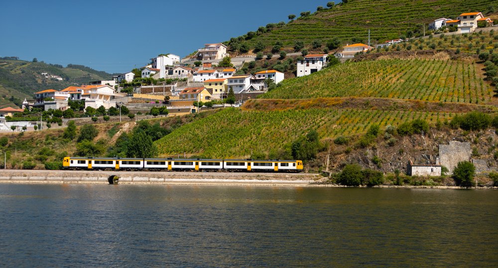 Yellow train passing in Douro railway with vineyards as background and the river in the foreground