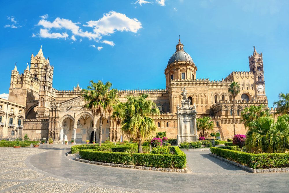 The beautiful Palermo cathedral with palm trees, arches, clock tower, etc. all visible on a bright day in summer in Palermo.