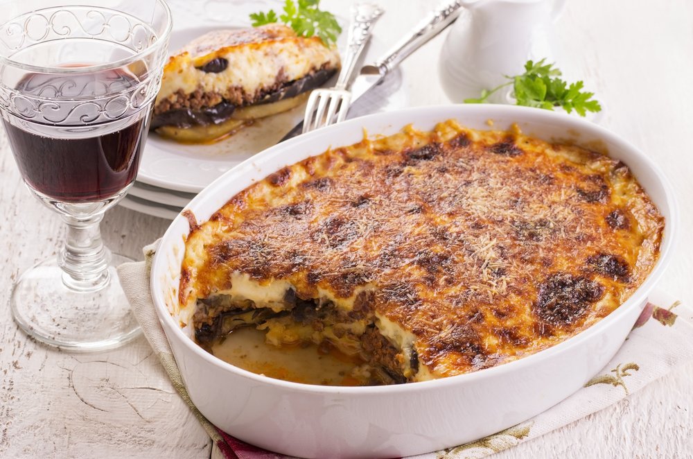 Moussaka with one serving cut out and put on a plate, with a glass of red wine to drink with it.