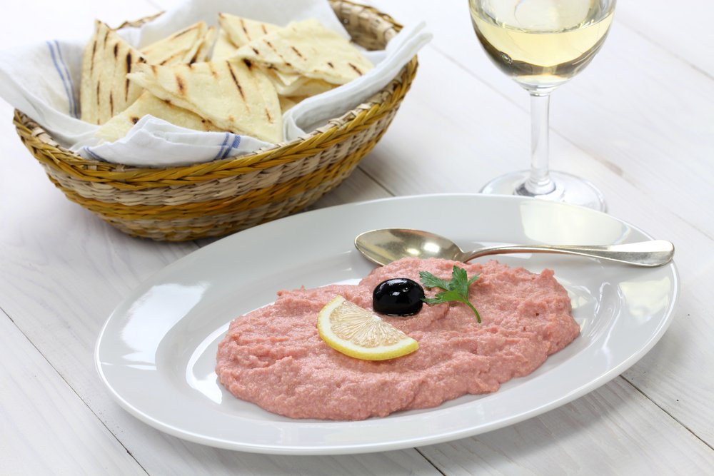 A pinkish colored dip that is made with fish roe, lemon and olive on top, a side of pita, and white wine.