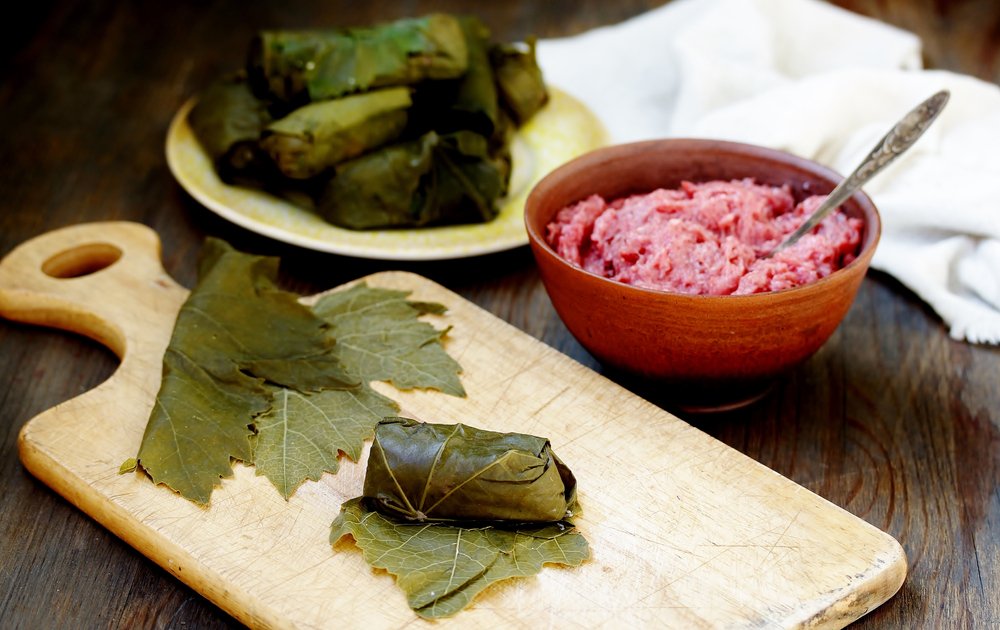 Ingredients to make dolma, stuffed wrapped grape leaves, with leaves and filling shown and a cutting board