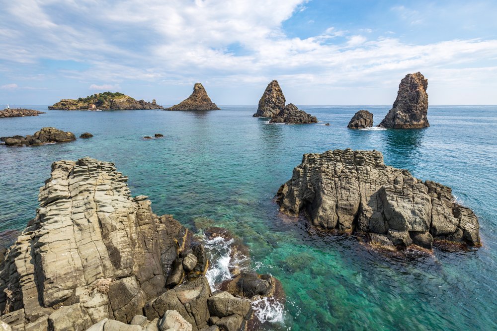 View on the rocky islands in Aci Trezza, Sicily, Italy, with the Islands of the Cyclops in the background.
