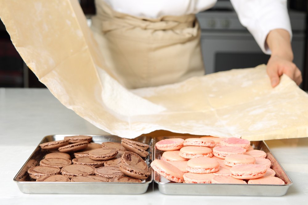 A chef preparing macaron cookie shells, some in a pink color (strawberry) and some in a brown color (chocolate) with wax paper