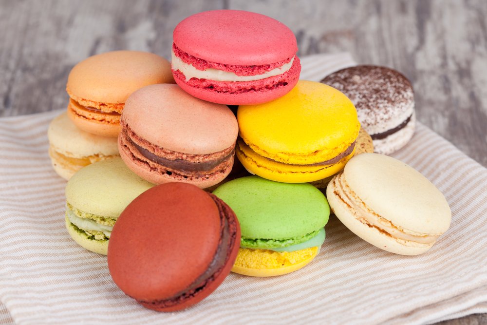 A pile of colorful macarons on a dish towel, including pink, yellow, pastel colored macarons, etc.