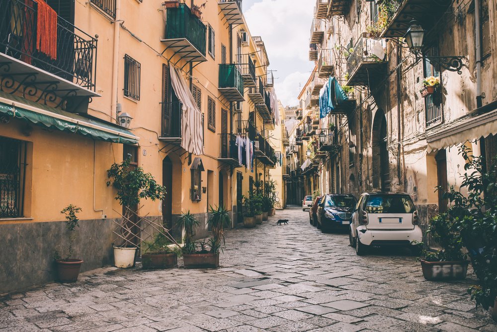 A narrow street in Palermo, Sicily with cars, balconies, clothing, cobblestone street