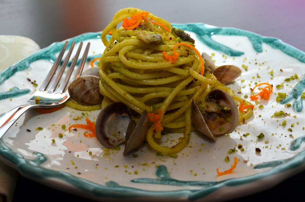 Dish of Spaghetti with clams and pistachios, a typical Sicilian cuisine dish, served on a white and turquoise plate