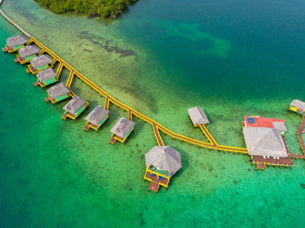 Aerial view of the punta caracol aqua lodge with lots of bungalows and bright yellow handrails on the raised boardwalk above the water