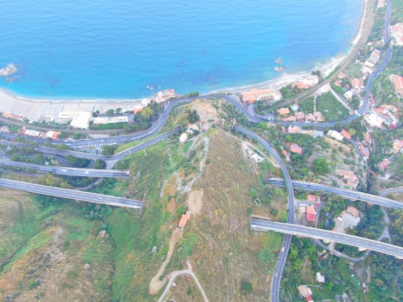 Aerial view of several different motorways in Sicily, some going through mountains via tunnels, and view of the beach and Sicilian landscape alongside the motorways.