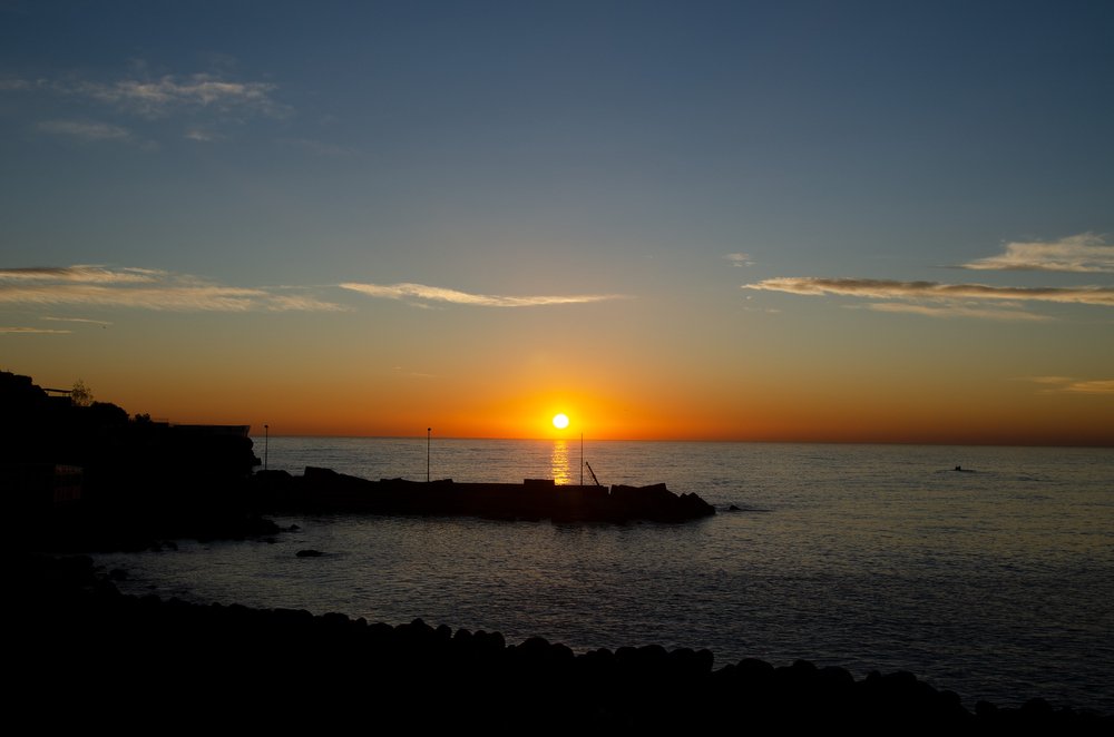 A sunset on the beach of San Giovanni Licuti with sandy beach, boat, peaceful water with few waves, and just a few clouds in the sky.