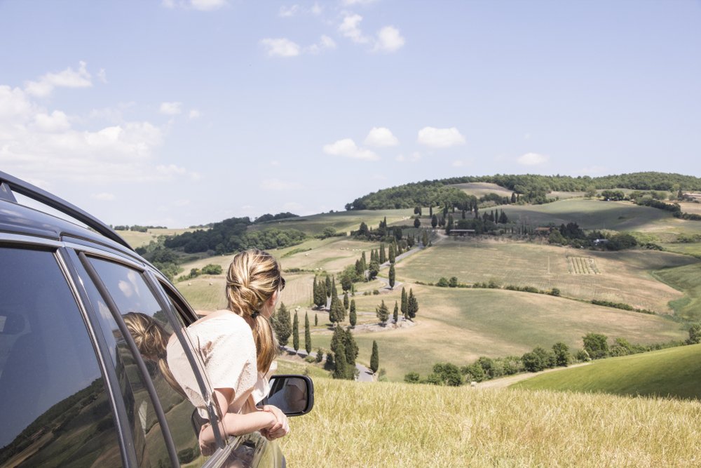 A woman hanging out of the passenger window to take in the view from a Tuscan road