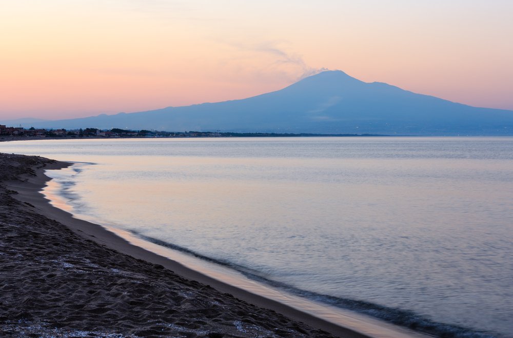 Beautiful sunset twilight on Agnone Bagni sea beach with smoky Etna volcano in far