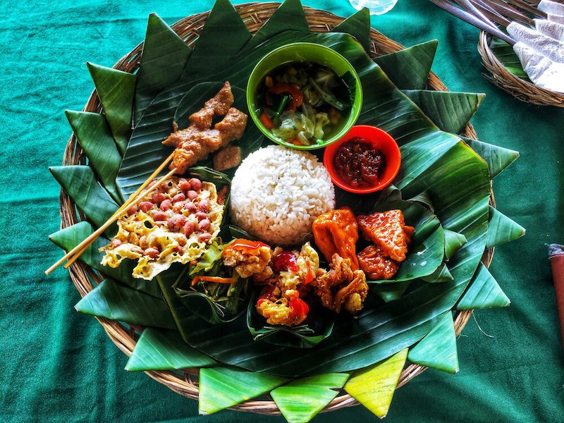 a blue tablecloth with a beautifully plated serving platter of different balinese dishes on it