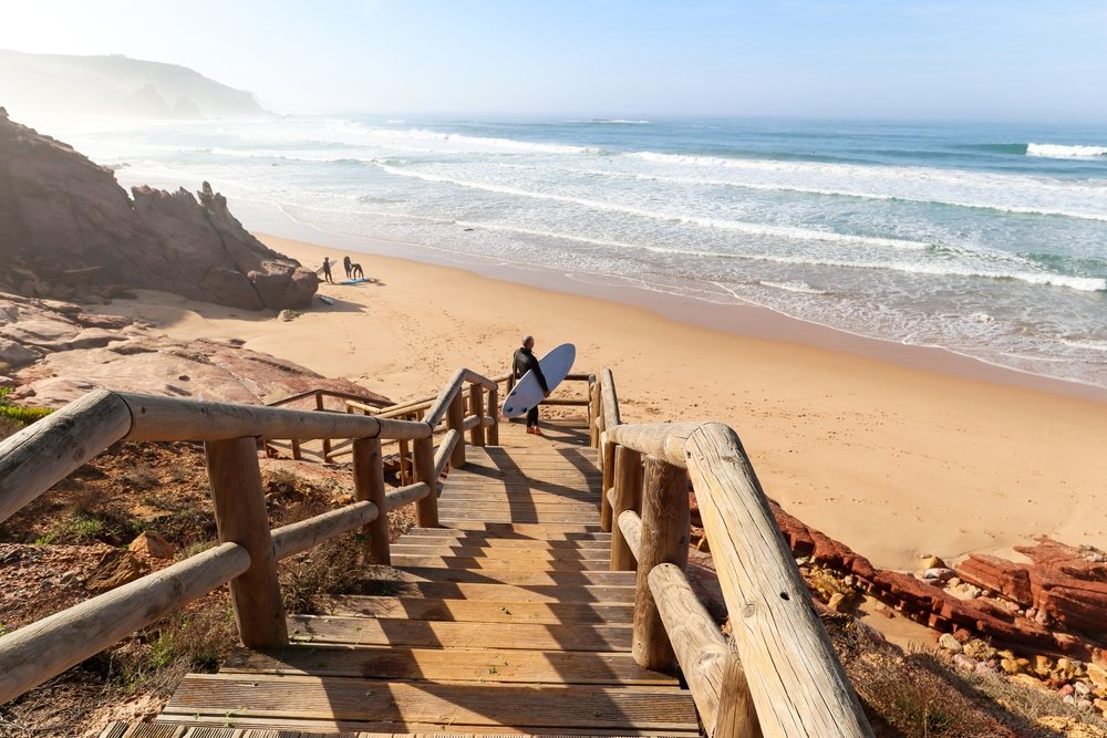  A surfer on the stairway going down to the beach of Praia de Odeceixe, a few other surfers on the beach but it is otherwise uncrowded and peaceful