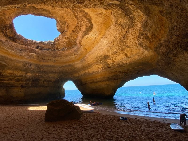 the view of the benagil caves in portugal on the algarve coast with several openings to the sea and sky and some people visiting with kayaks