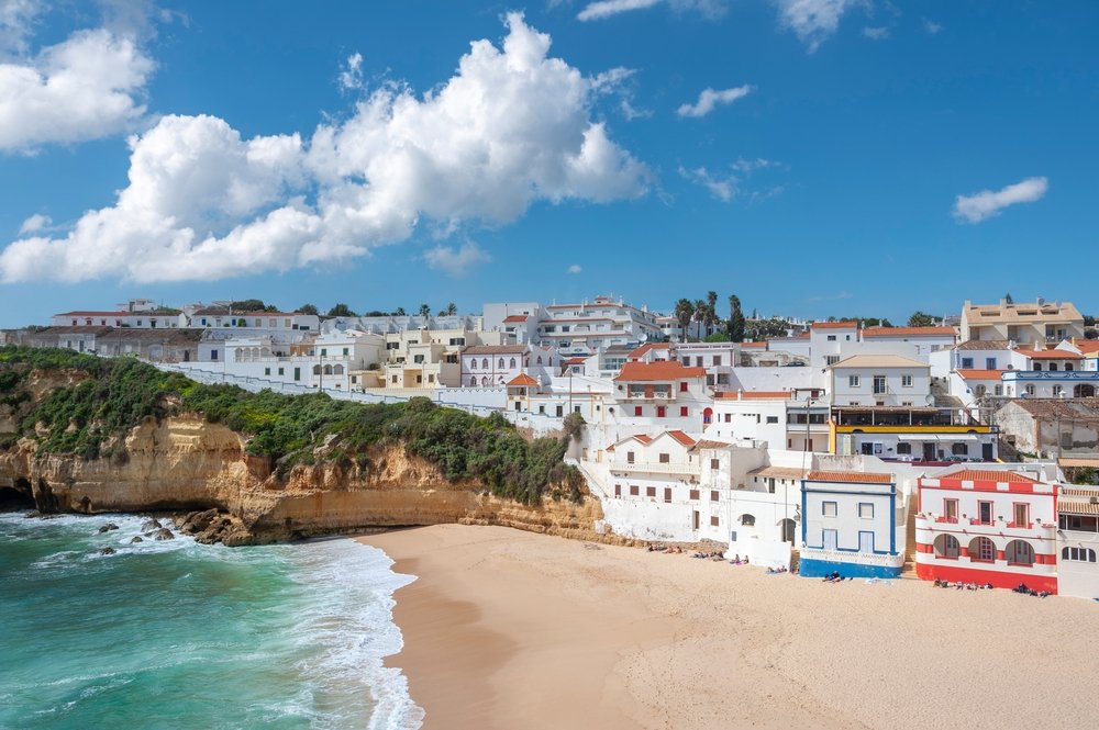 City near the beach in Carvoeiro in the Algarve in Portugal, rocky coastline, soft sand, white-washed houses with colorful blue, red, and yellow details.