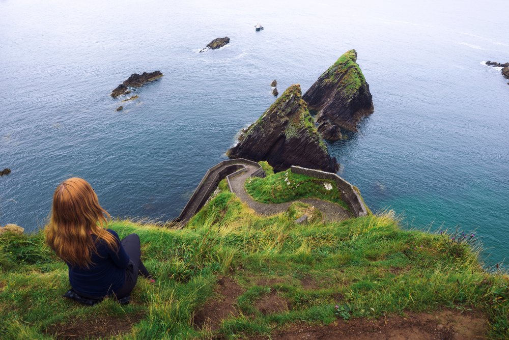 Redheaded woman sitting in front of a narrow path down leading to the water