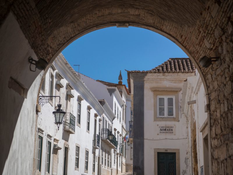 Stone archway revealing the rest of Faro old town with white walls and gray stonework 