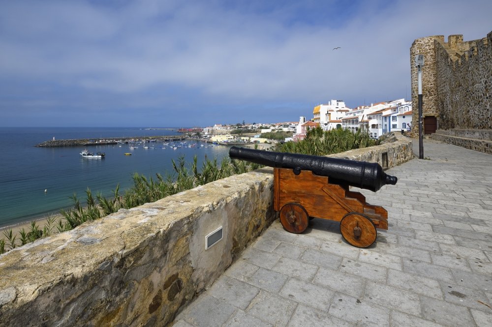 the fortress in sines portugal with a cannon pointing out to sea on a mostly clear day with the city visible in the background