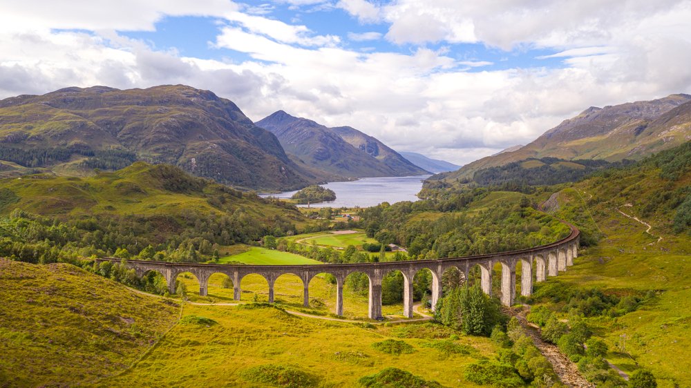 Glenfinnan Viaduct in front of a lake in scotland, a famous train route