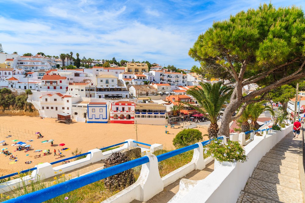 Colorful beach houses with tourists on the beach sands at Algarve, Portugal in the town of Carvoeiro, a popular Algarve destination