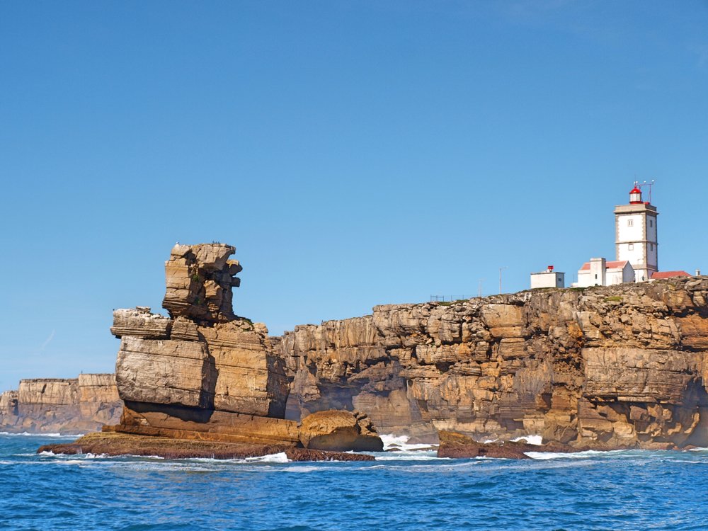 The Cabo Carveiro light house which is white and red on the rocky outcropping near the sea on the coast of Portugal near Peniche