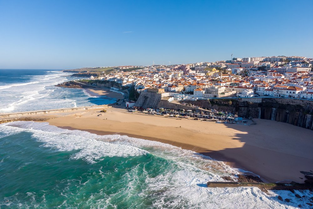 View of the beach in Ericeira as well as the houses of the town along the coast on a sunny day in Portugal