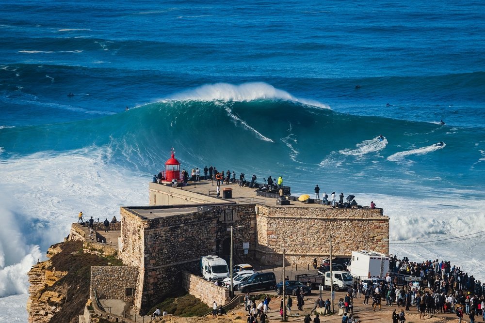 Surfers on the giant wave in Nazare with a large crowd watching