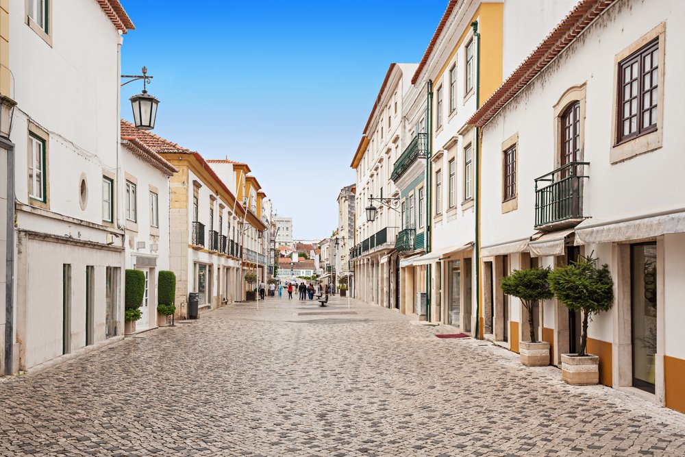 Tomar city center, with a cobblestone-style street, people walking in the distance, and white buildings.