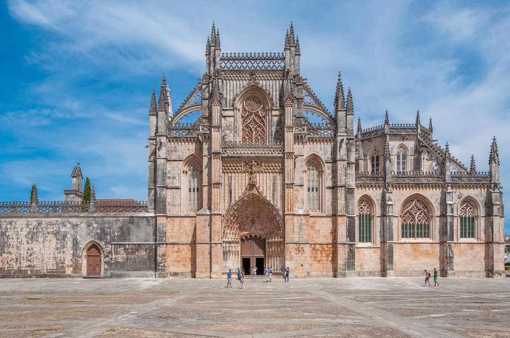 The large ornate facade of the Monastery de Batalha, the battle monastery, with lots of architectural detailing and arches and spires