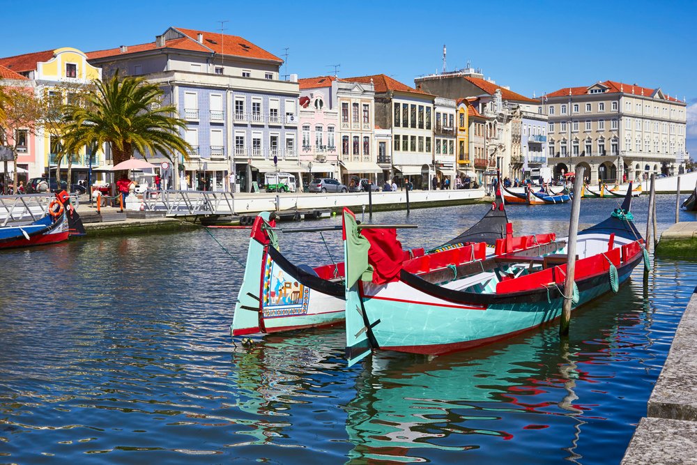 Aveiro city center with teal and red boats in the canal with pastel colored buildings on the other side of the river