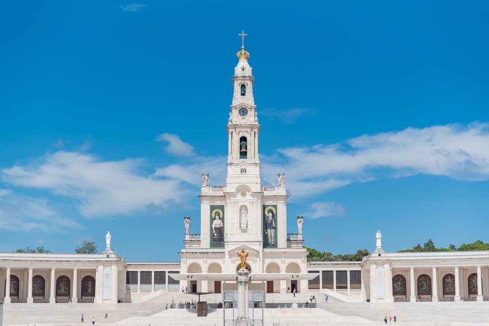 Massive sanctuary of our lady of Fatima in Portugal, a white church building with a gold jesus statue in front