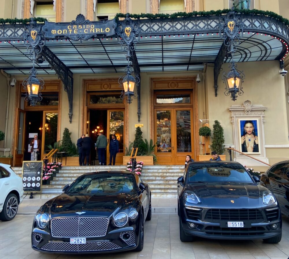 Expensive cars parked in front of the famous Monte Carlo Casino, one of the most famous casinos in the world. Everything looks very luxurious and expensive.