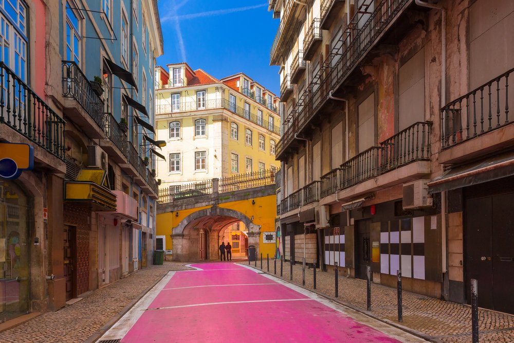 the pink street of lisbon, with a pink pedestrian walkway going underneath a bridge and buildings in the background