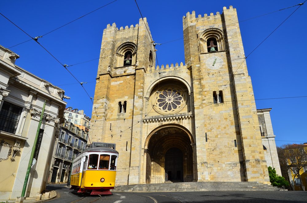 Lisbon cathedral in stone with the famous yellow tram running front of it on a sunny day with no tourists in sight