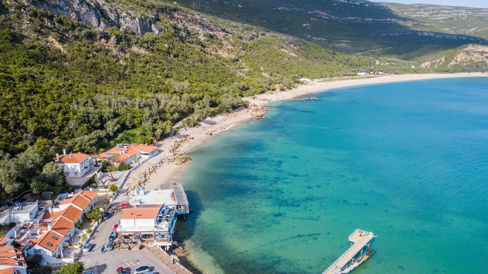 Aerial view of Portinho da Arrábida beach, in Setúbal, Portugal, with brilliant turquoise water and white houses with terra cotta red roofs