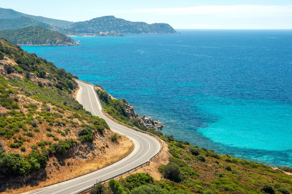 Sardinia landscape with an empty road and brilliant blue and dark azure waters in the sea, with dramatic coast scenery