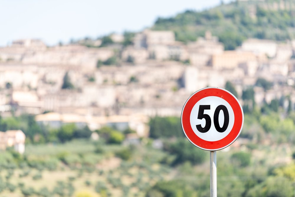 A sign showing that the speed limit is 50 km per hour with a blurry city in the background