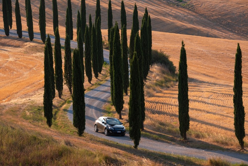 Famous winding road with a car driving in Tuscany, Italy in summer with dry fields that have recently been razed