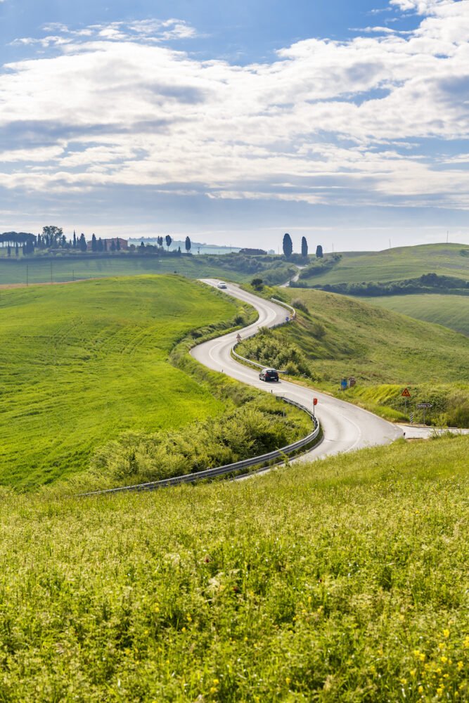 Winding country road in rural landscape with cars, view of town in the distance beyond the road
