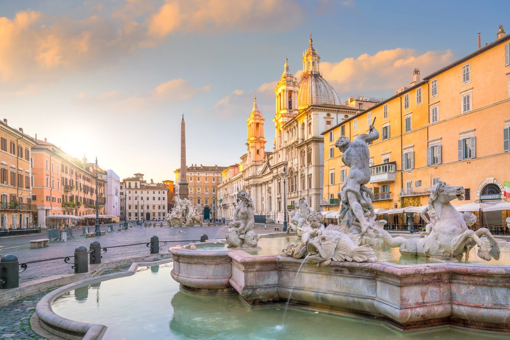 The historic square of Piazza Navona with its famous fountain and beautiful buildings behind it as seen around sunset as the sun dips behind the buildings in Rome