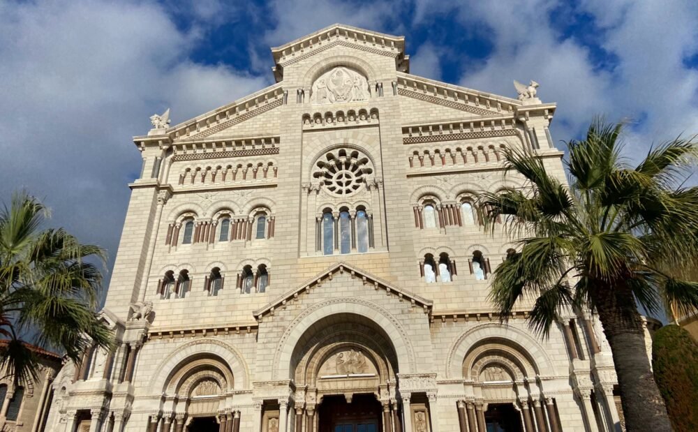 The white marble facade of Saint Nicholas Cathedral, flanked by palm trees, on a sunny day with some clouds. This church was built in the 19th century and reflects a more modern style.