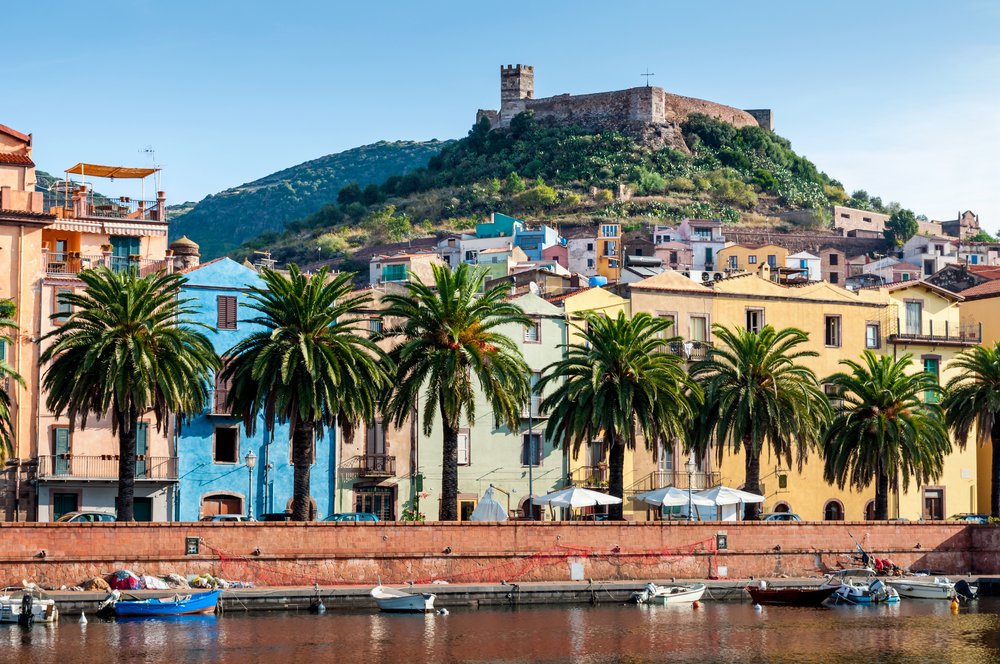 the colorful inland town of bosa on the riverfront with colorful houses and a hill with ruins