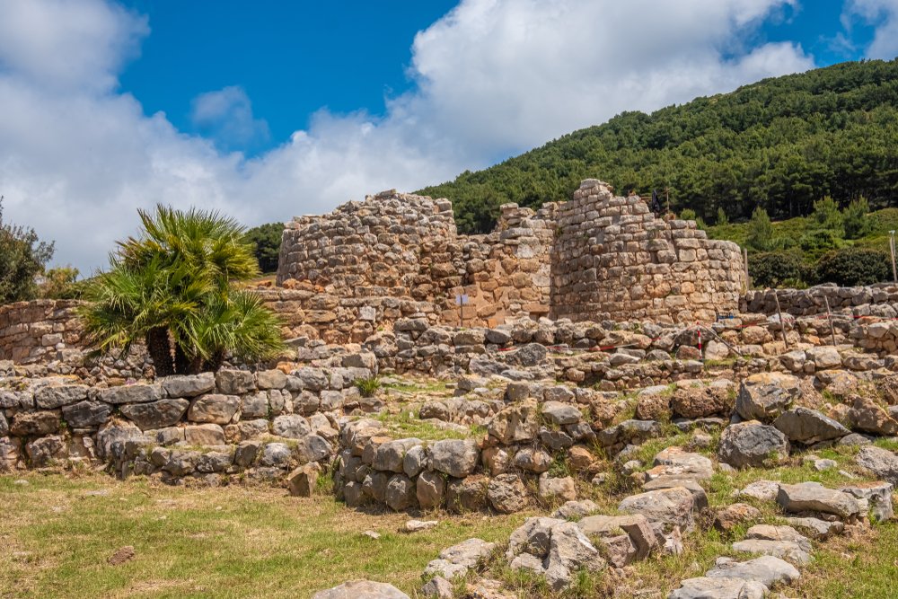 Stone ruins of a Nuragic settlement, the people who lived on Sardinia in the past, and green landscape on a partly cloudy day