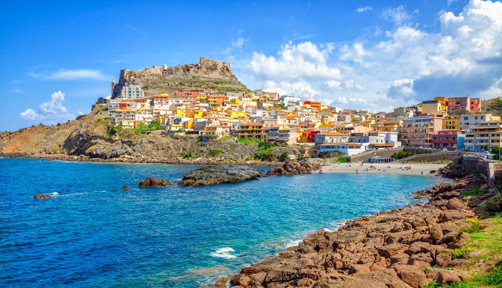 View of the beach of Castelsardo with the colorful buildings going up the hill and the castle at the top of the town